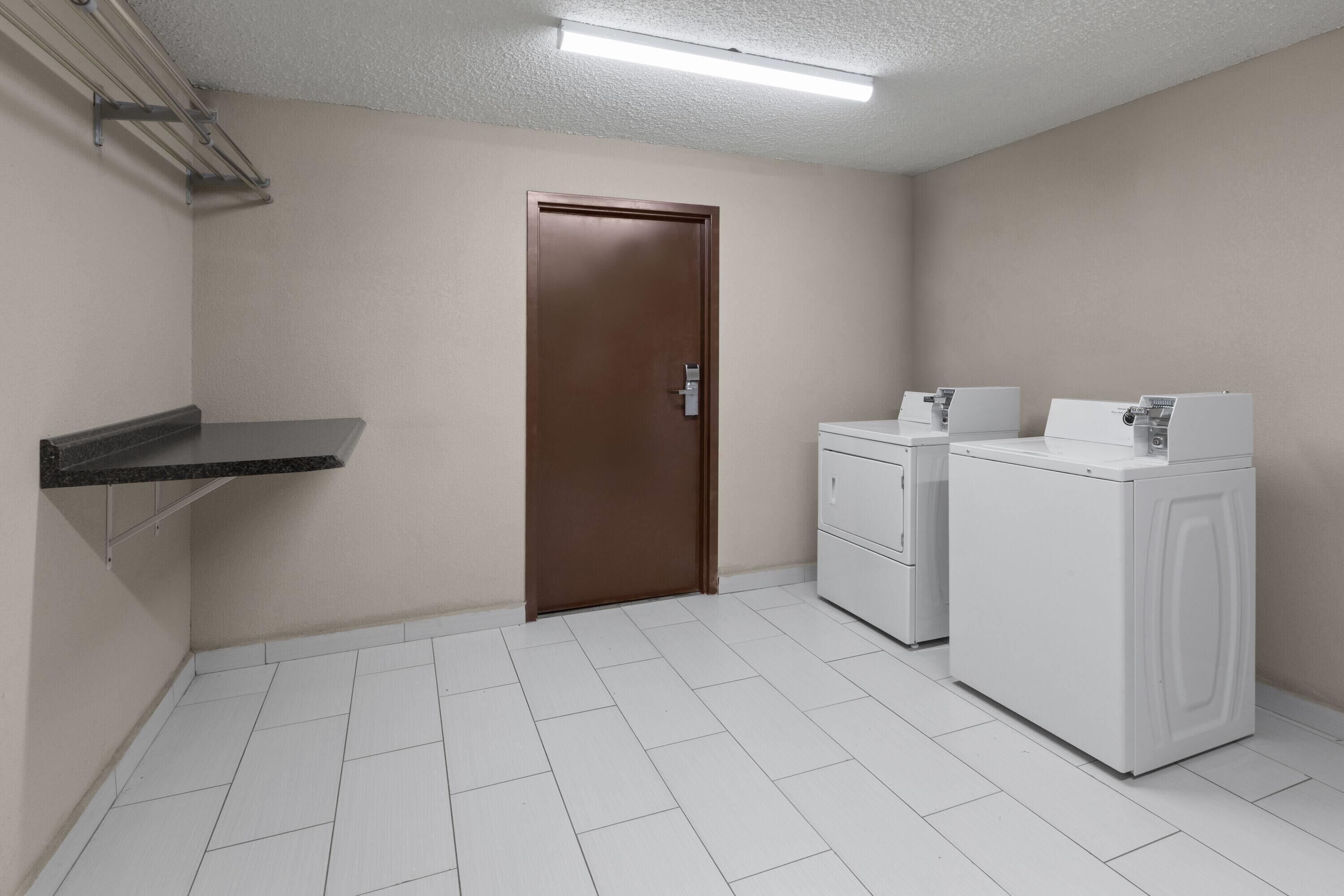 Una sala de lavandería con una puerta marrón, una lavadora blanca y un estante.
