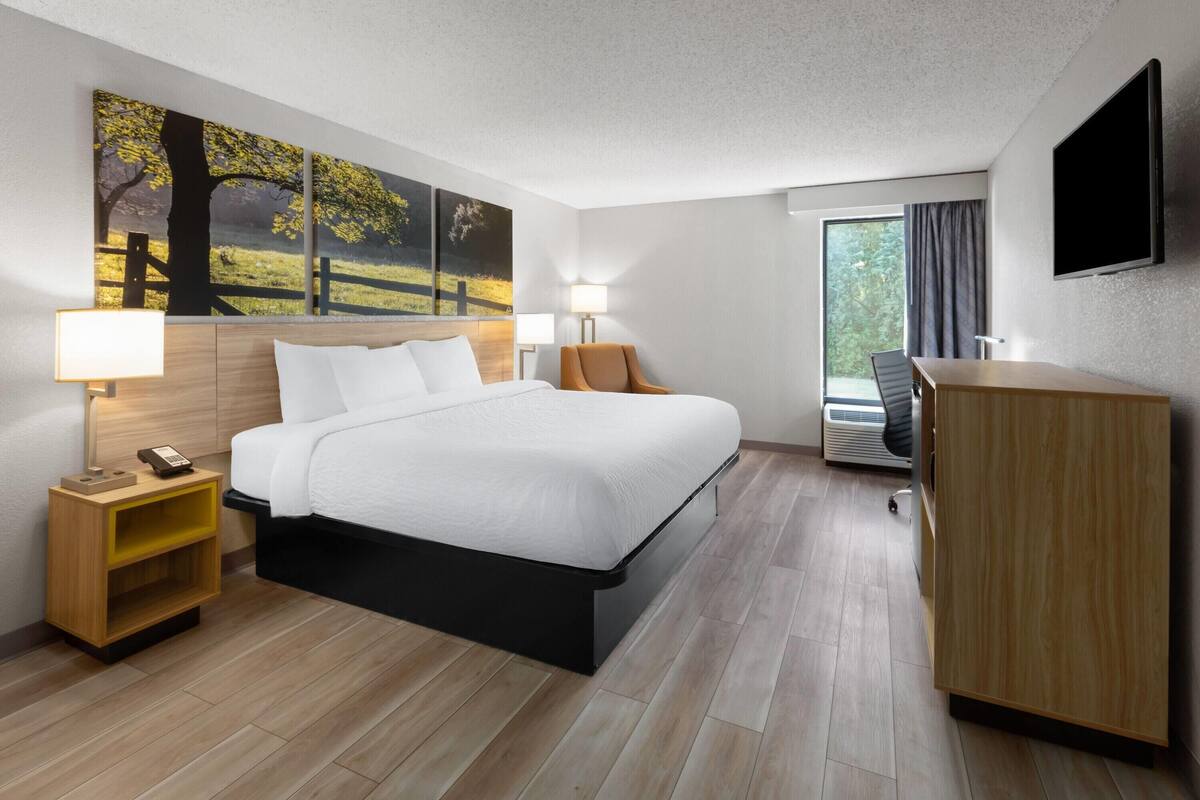 Een hotelkamer met een bed, nachtkastjes, een bureau, een stoel, een televisie en een raam met gordijnen.