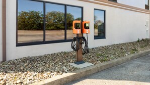 Ein modernes Gebäude mit zwei orangefarbenen Ladestationen für Elektrofahrzeuge, die an einer Wand angebracht sind, umgeben von einem Kiesbereich.