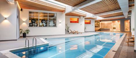 An indoor swimming pool with clear blue water, wooden ceiling beams, and a modern design.