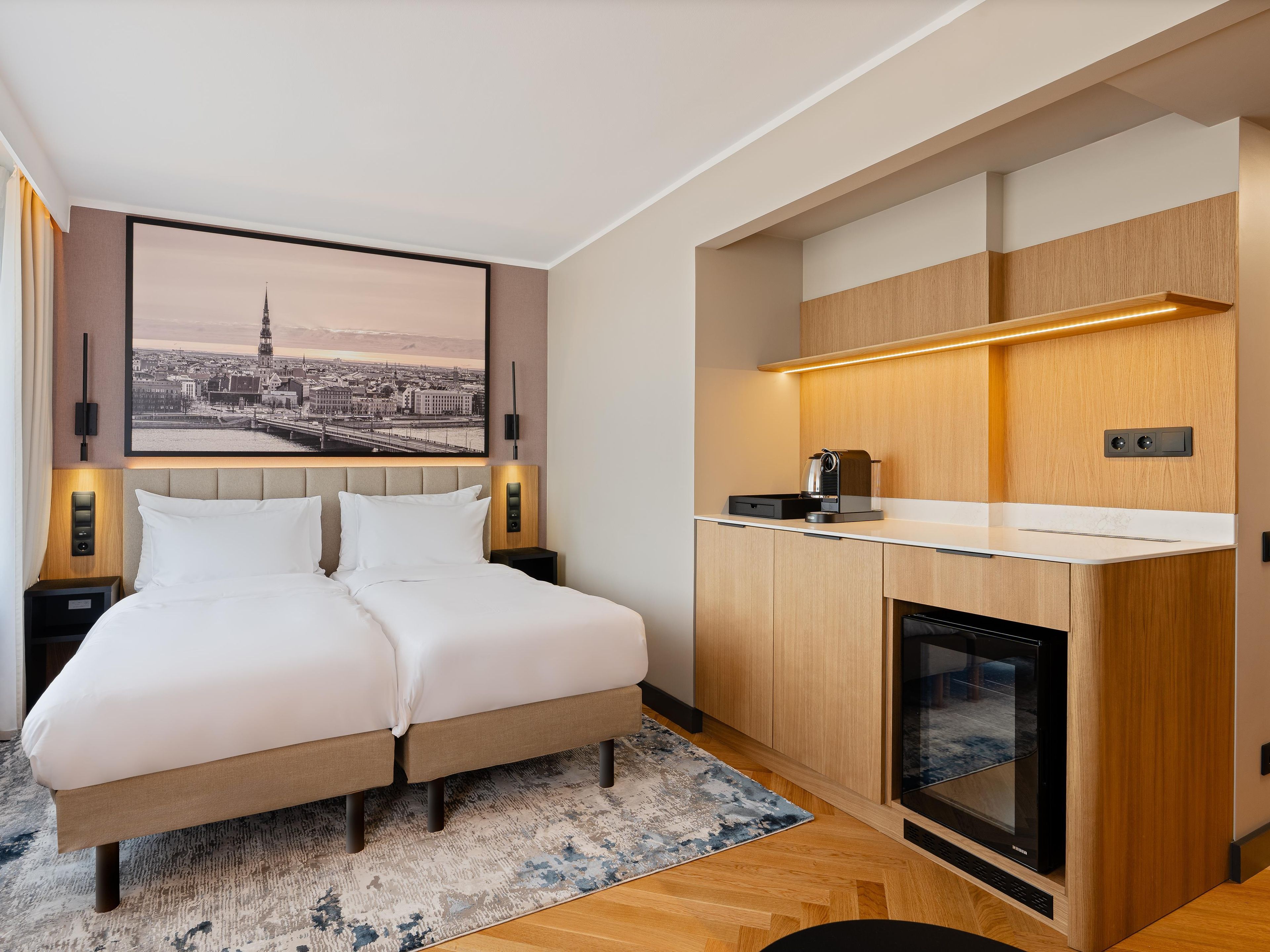 A hotel room with a bed, a cityscape painting, a coffee machine, and a built-in oven.