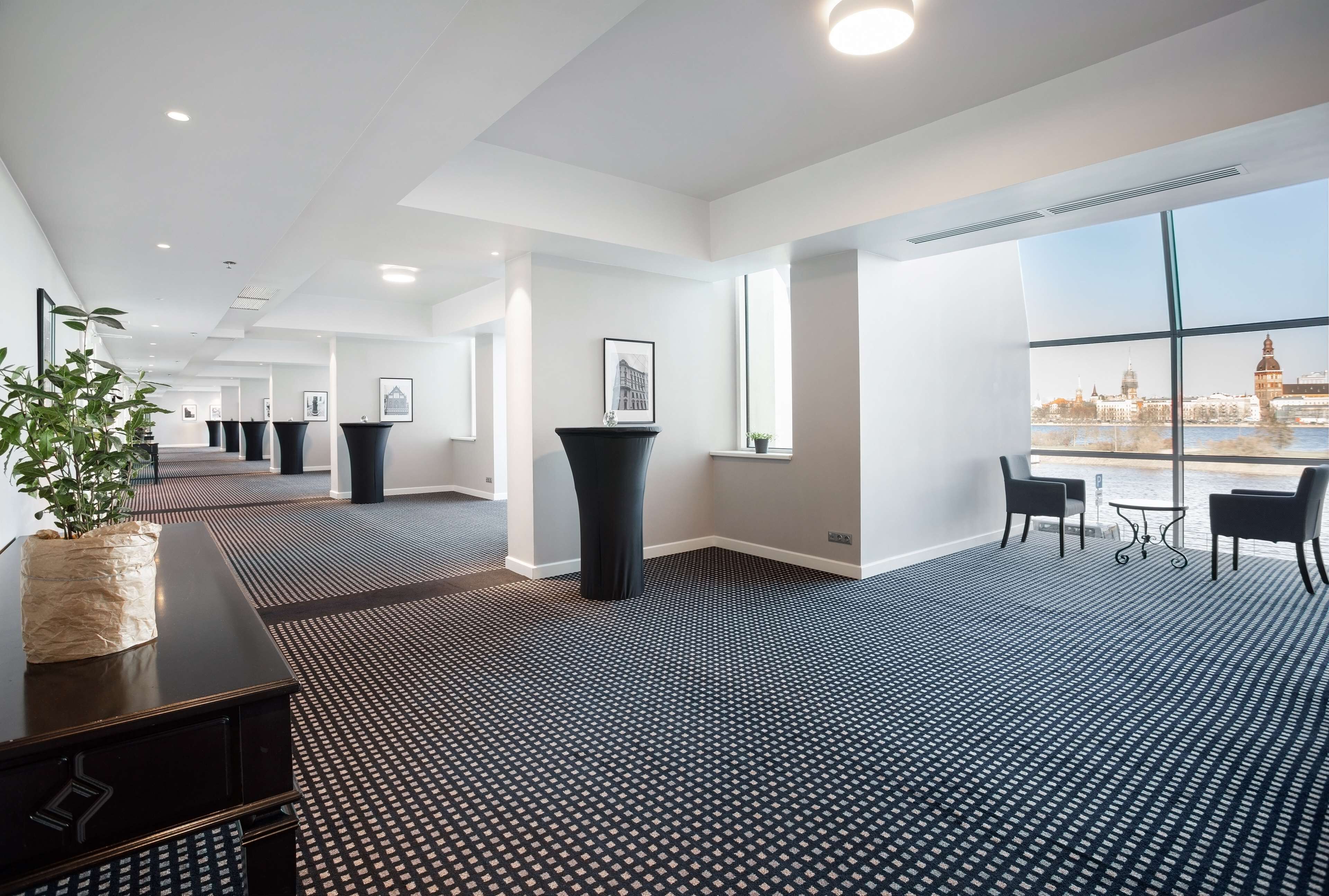 A modern hotel lobby with a patterned floor, a large window offering a city view, a reception desk, and a seating area.