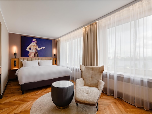 Una habitación de hotel con una cama grande, una silla, una mesa redonda y un cuadro en la pared.