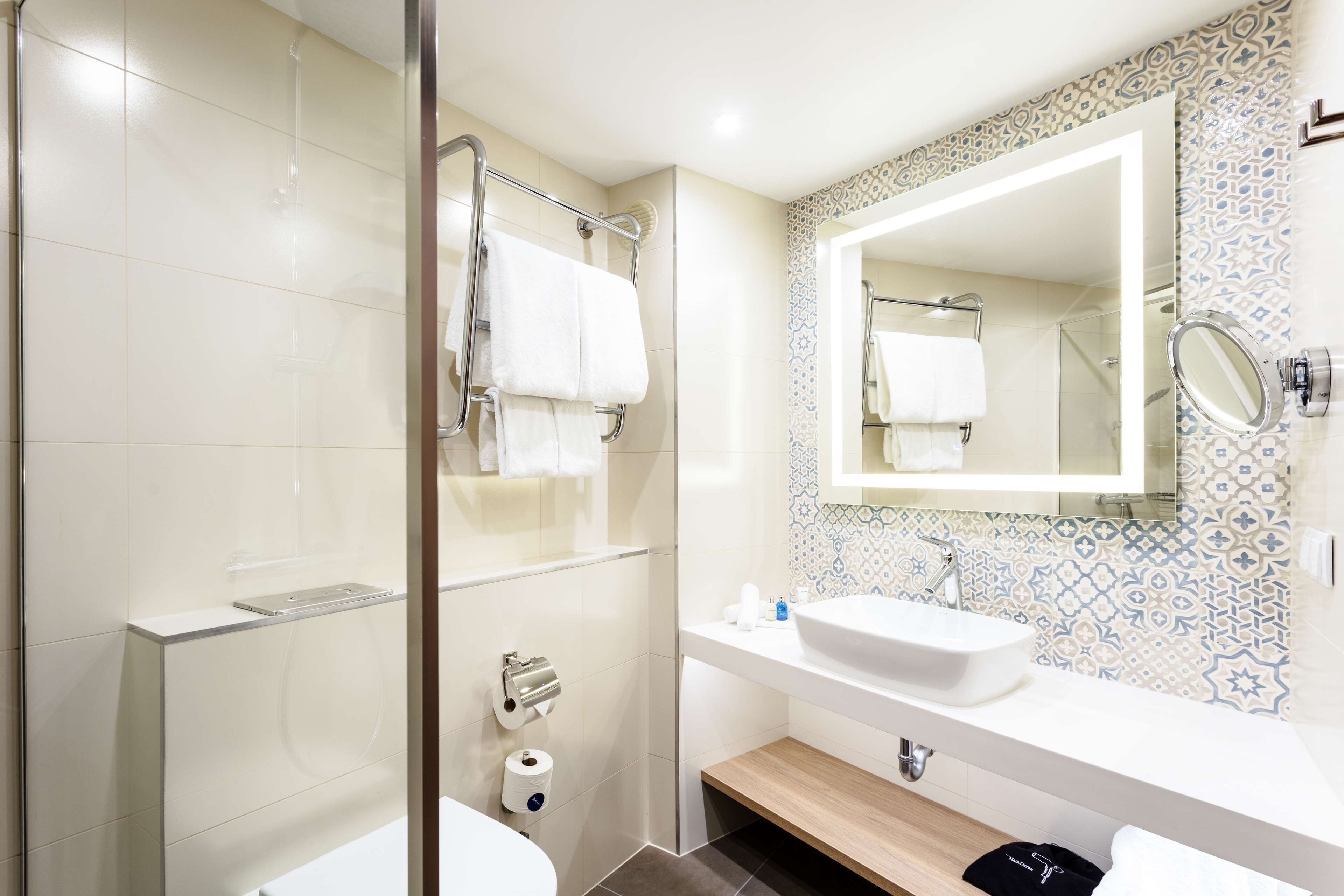 A modern bathroom with a glass shower enclosure, a white sink, and a mirror with a decorative backsplash.