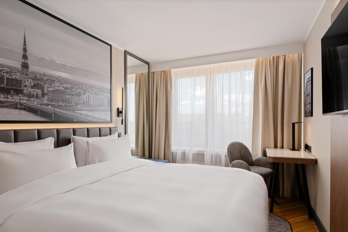 Een hotelkamer met een groot bed, een bureau, een stoel en uitzicht op de stad.