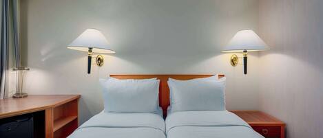 Quarto de hotel com duas camas, cabeceira de madeira, mesas de cabeceira e luminárias fixadas na parede.