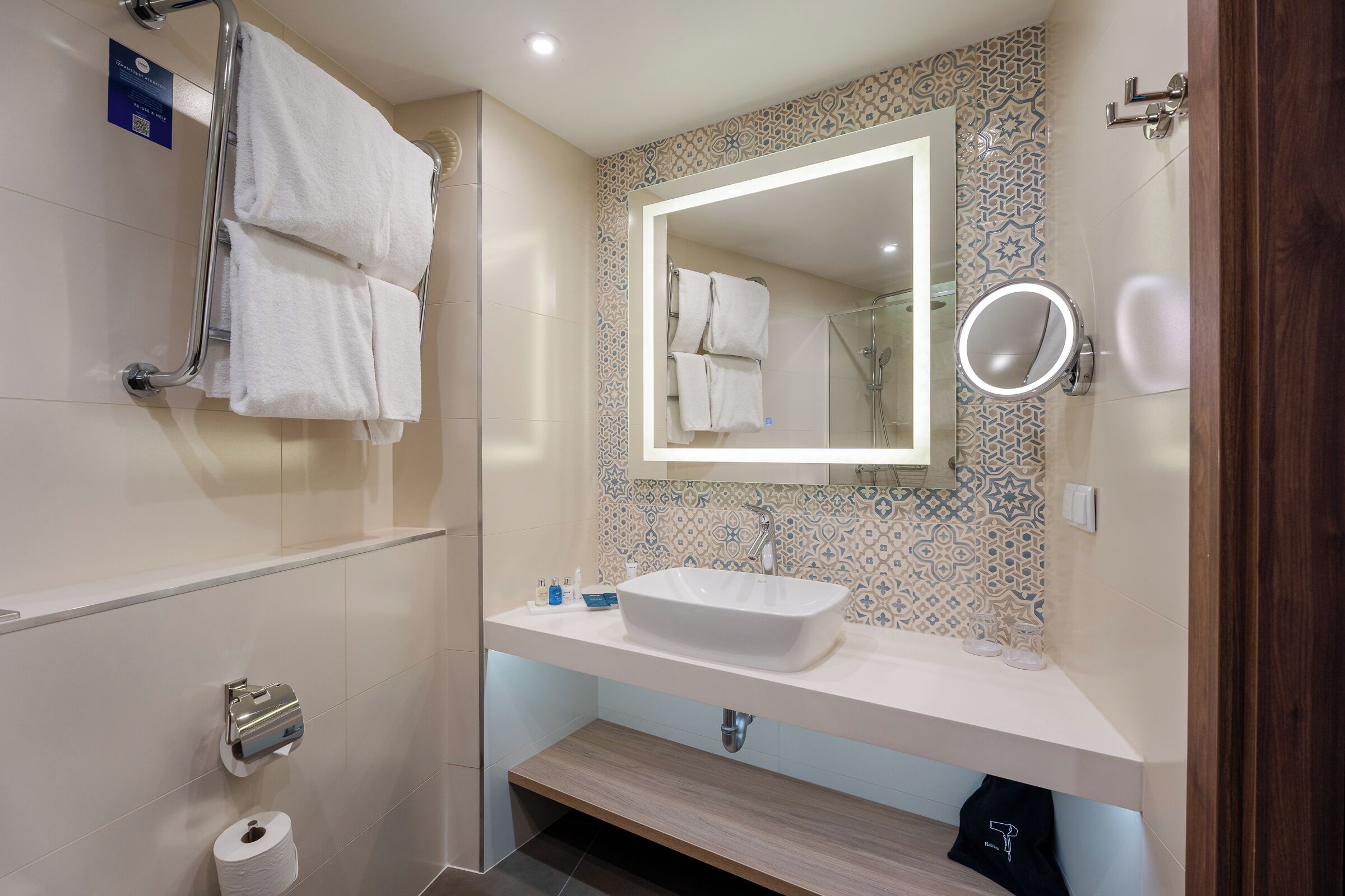A modern bathroom with a large mirror, a sink, and a towel rack.