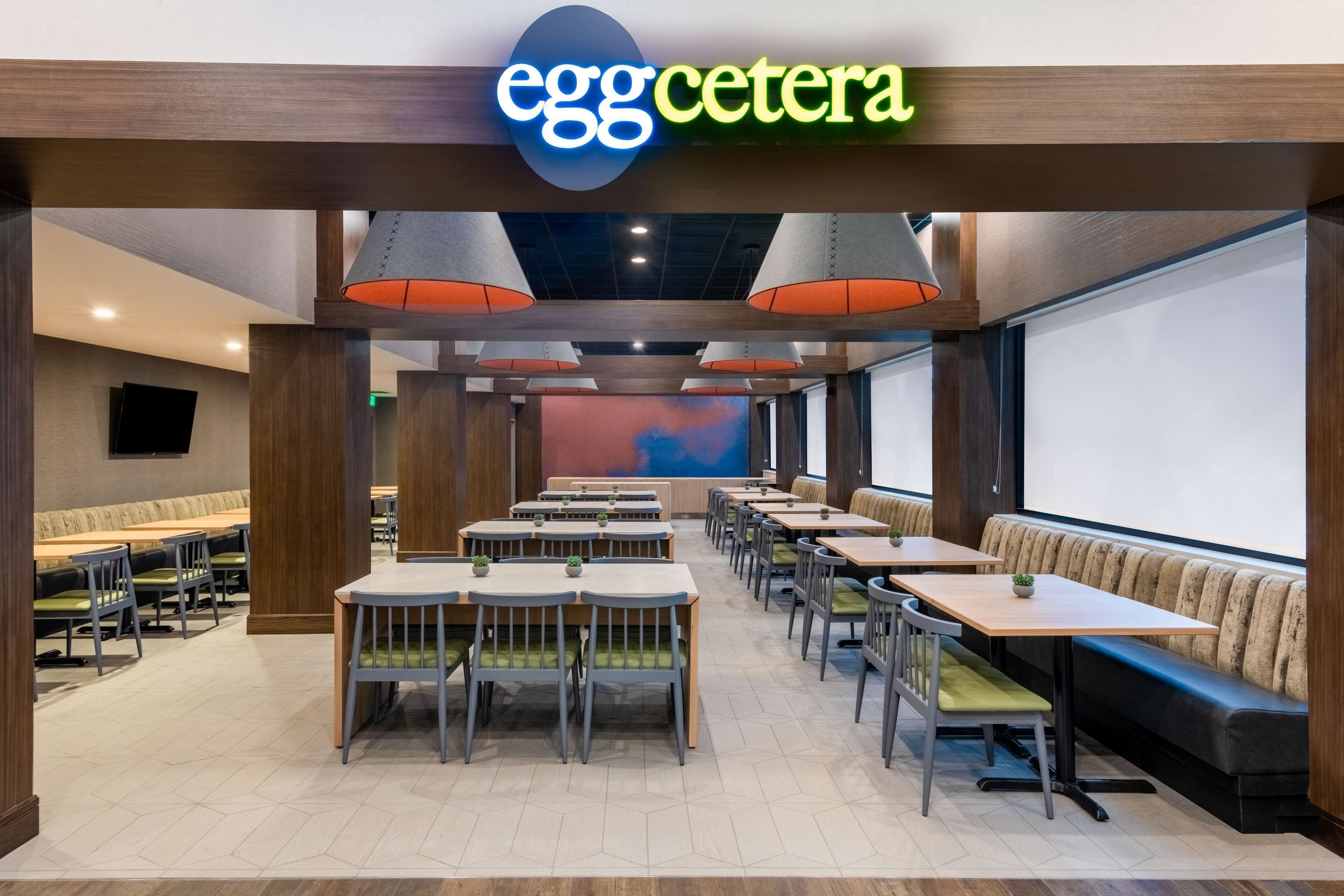 A restaurant interior with a modern design, featuring a long counter with booths, pendant lighting, and a large screen wall.