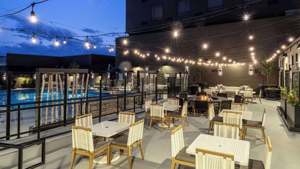 An outdoor patio with tables and chairs, a pool, and string lights. - DoubleTree by Hilton Denver Cherry Creek (Denver)