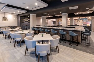Un restaurante moderno con zona de bar, diversas opciones de asientos, incluyendo taburetes y mesas, y una decoración interior contemporánea.