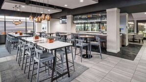 A modern restaurant with multiple dining tables and chairs, a bar area with shelves of bottles, and a large window providing a view of the city. - DoubleTree by Hilton Denver Cherry Creek (Denver)