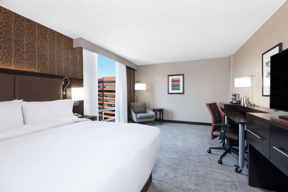 A hotel room with a large bed, a desk with a chair, a small table, and a TV.