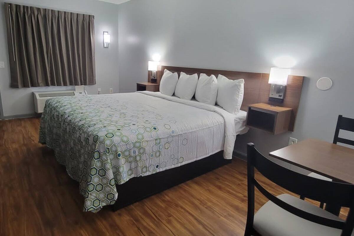 A hotel room with a bed, bedside tables, a desk, a chair, and a window with curtains.
