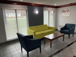 Un área de espera con un sofá amarillo, dos sillones, una mesa de centro de madera y una lámpara de pared.