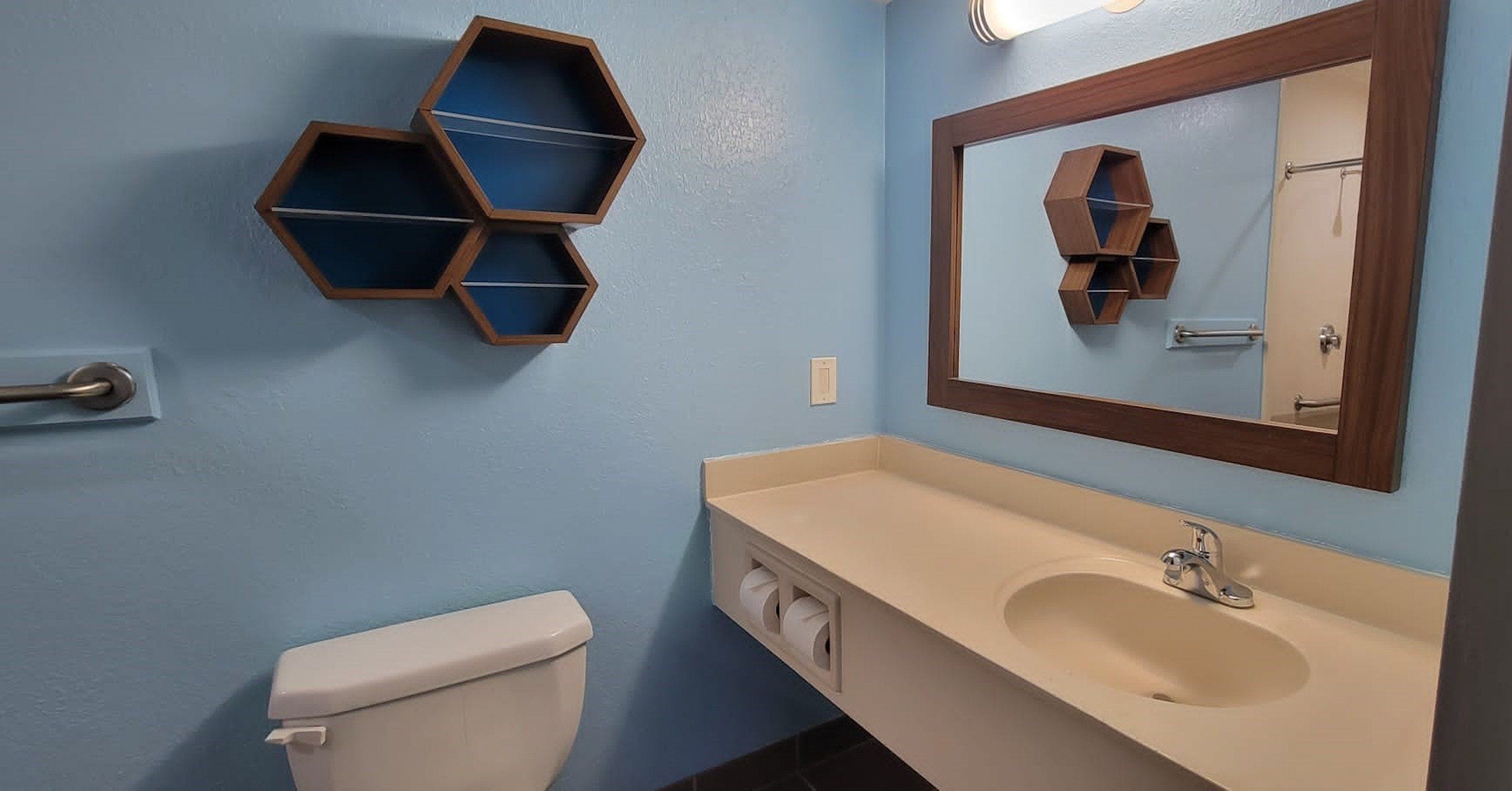 Un baño con inodoro, lavamanos con espejo y estantes hexagonales en la pared.