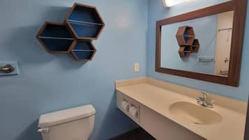 Un baño con inodoro, lavamanos con espejo y estantes hexagonales en la pared.