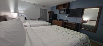 Habitación de hotel con dos camas, televisión, espejo y kitchenette.