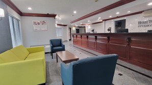 A hotel lobby with a reception desk, a yellow sofa, a blue armchair, and a wooden coffee table. - HomeTowne Studios By Red Roof Egg Harbor–Atlantic City Airport (Egg Harbor Township)