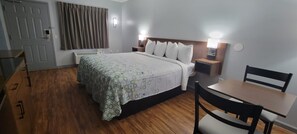 A hotel room with a bed, bedside tables, a desk, a chair, and a window with curtains.