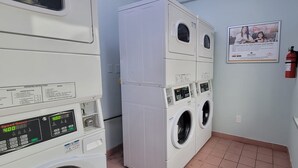 A laundry room with stacked washers and dryers, a fire extinguisher, and a poster on the wall. - HomeTowne Studios By Red Roof Egg Harbor–Atlantic City Airport (Egg Harbor Township)
