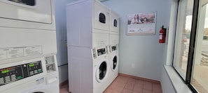 A laundry room with stacked washers and dryers, a fire extinguisher, and a poster on the wall.