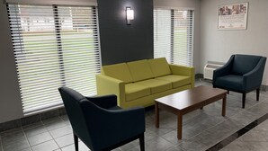 A waiting area with a yellow sofa, a blue armchair, and a wooden table. - HomeTowne Studios By Red Roof Egg Harbor–Atlantic City Airport (Egg Harbor Township)