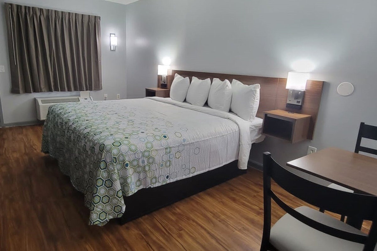 A hotel room with a bed, bedside tables, a desk, a chair, and a window with curtains.