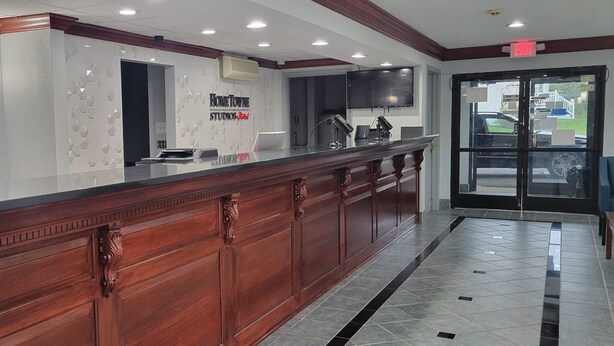A reception desk with a modern design, a flat-screen TV, and a sign for 'Home Towne Studios'. - HomeTowne Studios By Red Roof Egg Harbor–Atlantic City Airport (Egg Harbor Township)