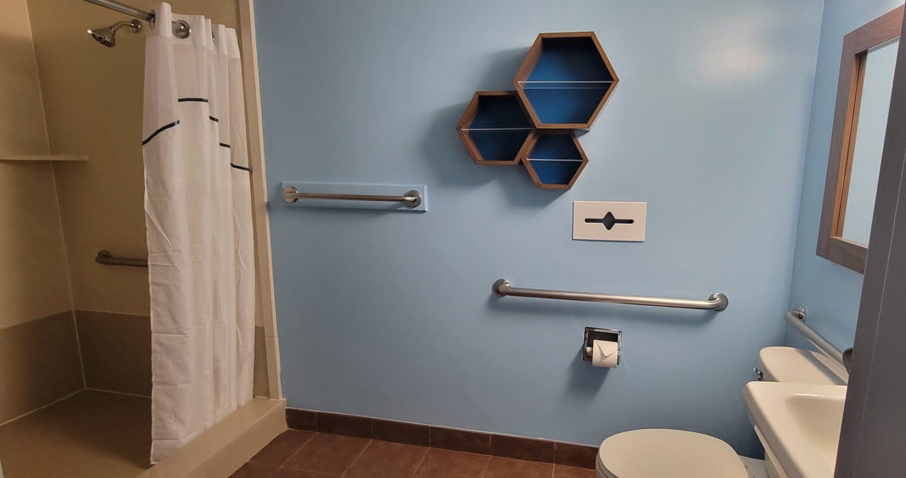 Un baño con pared azul, inodoro blanco, ducha con cortina blanca y baranda.