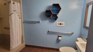 A bathroom with a blue wall, a white toilet, a shower with a white curtain, and a handrail.