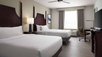 A hotel room with two beds, a desk, a chair, a television, and a ceiling fan.