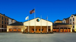 A hotel with a central building featuring a circular logo, multiple flags, and a well-lit entrance.