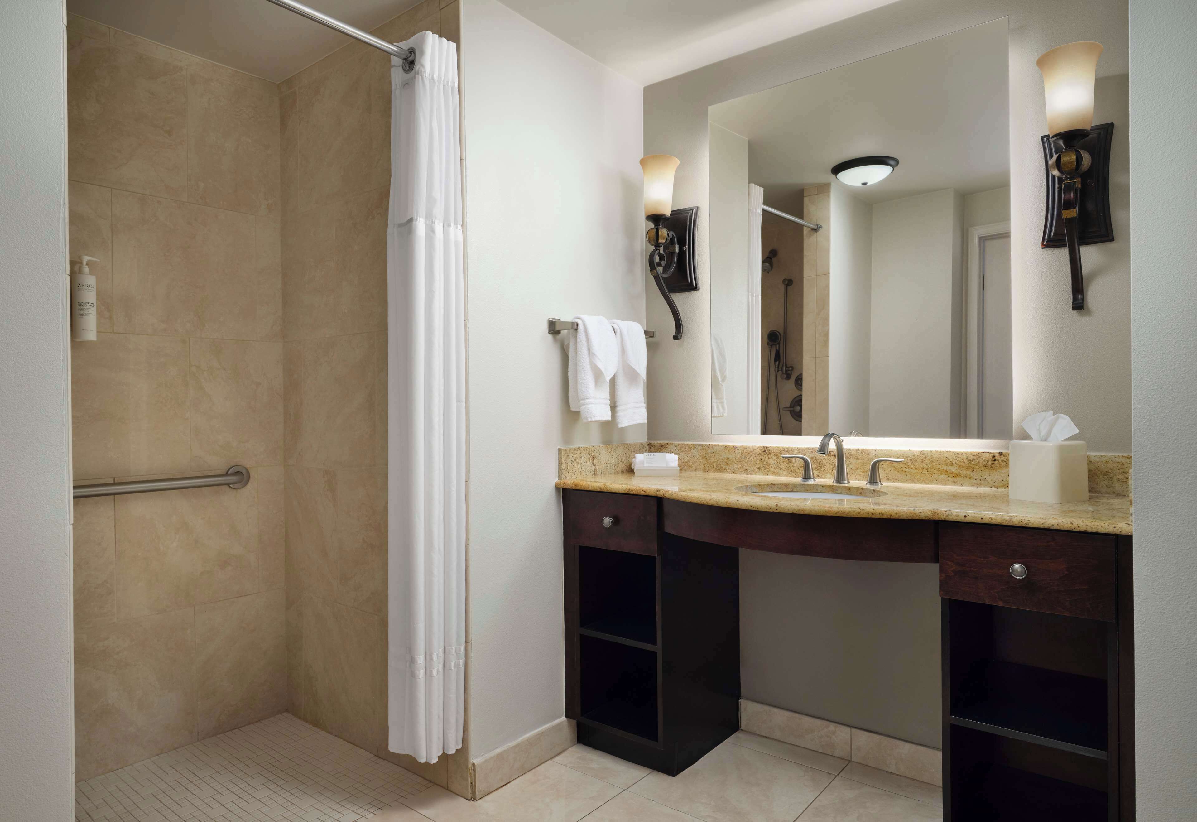 Un baño moderno con ducha, tocador y un espejo grande.