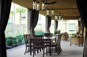Een buiten eethoek met een lange tafel en stoelen, omgeven door gordijnen en hangende lampen.