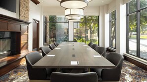 A conference room with a long table, multiple chairs, a fireplace, and large windows offering a view of greenery.