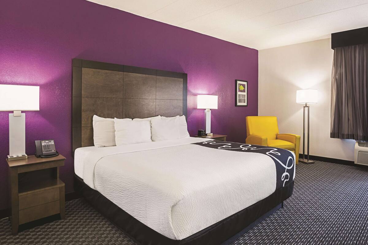 A hotel room with a large bed, two bedside tables with lamps, a chair, and a window with curtains.