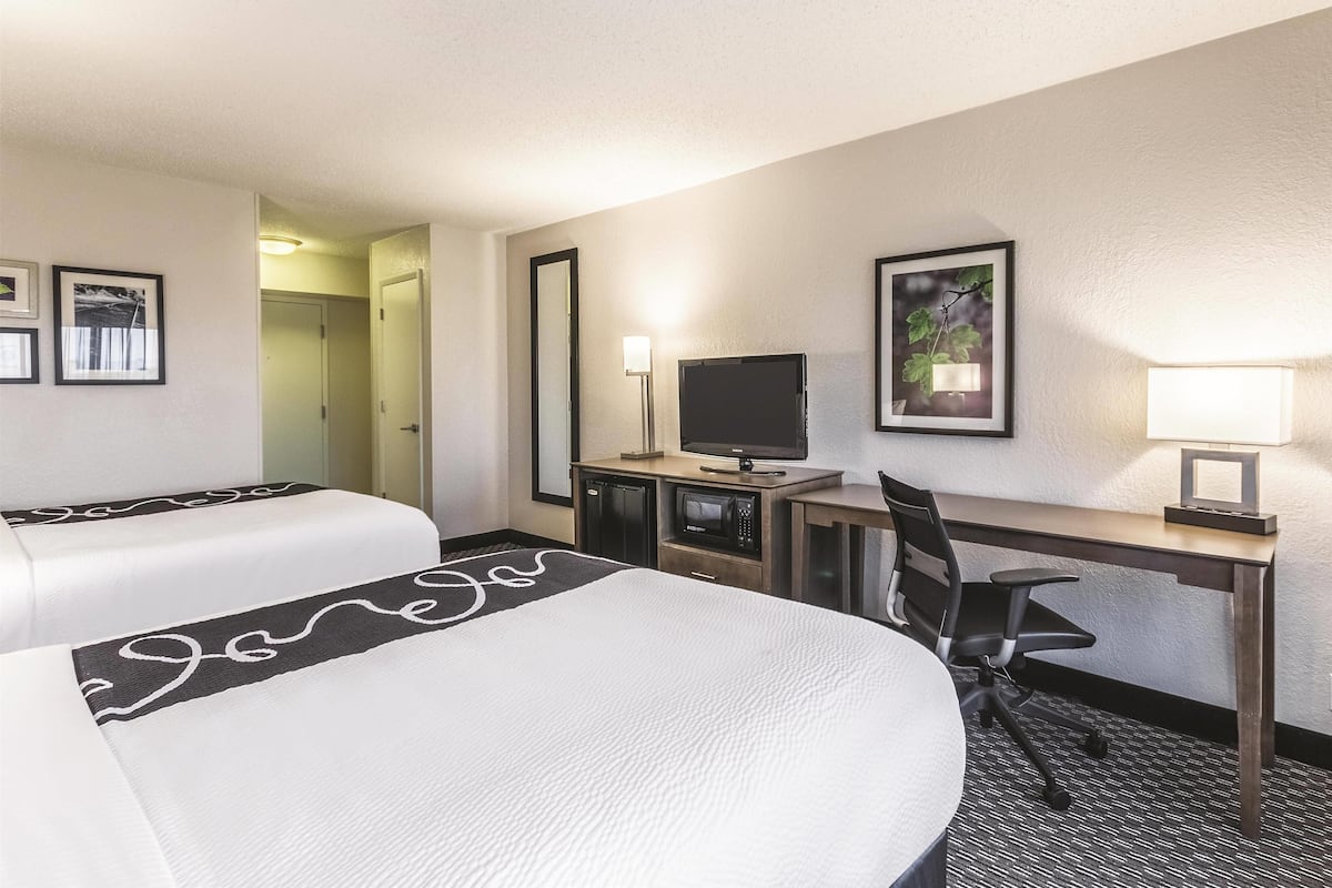 A hotel room with two beds, a desk with a computer, a TV, and a lamp.
