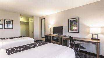 A hotel room with two beds, a desk with a computer, a TV, and a lamp.