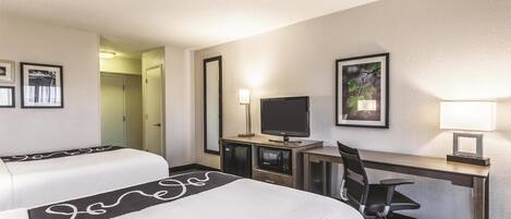 A hotel room with two beds, a desk with a computer, a TV, and a lamp.