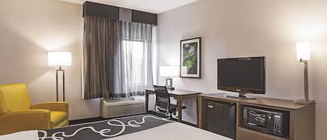 Ein Hotelzimmer mit einem Bett, einem Schreibtisch mit Computer, einem Sessel, einem Fernseher und einer Mikrowelle.