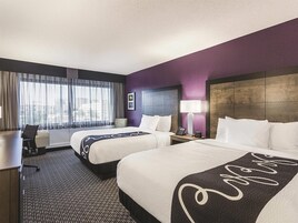 Habitación de hotel con dos camas, un escritorio y una ventana con cortinas translúcidas.