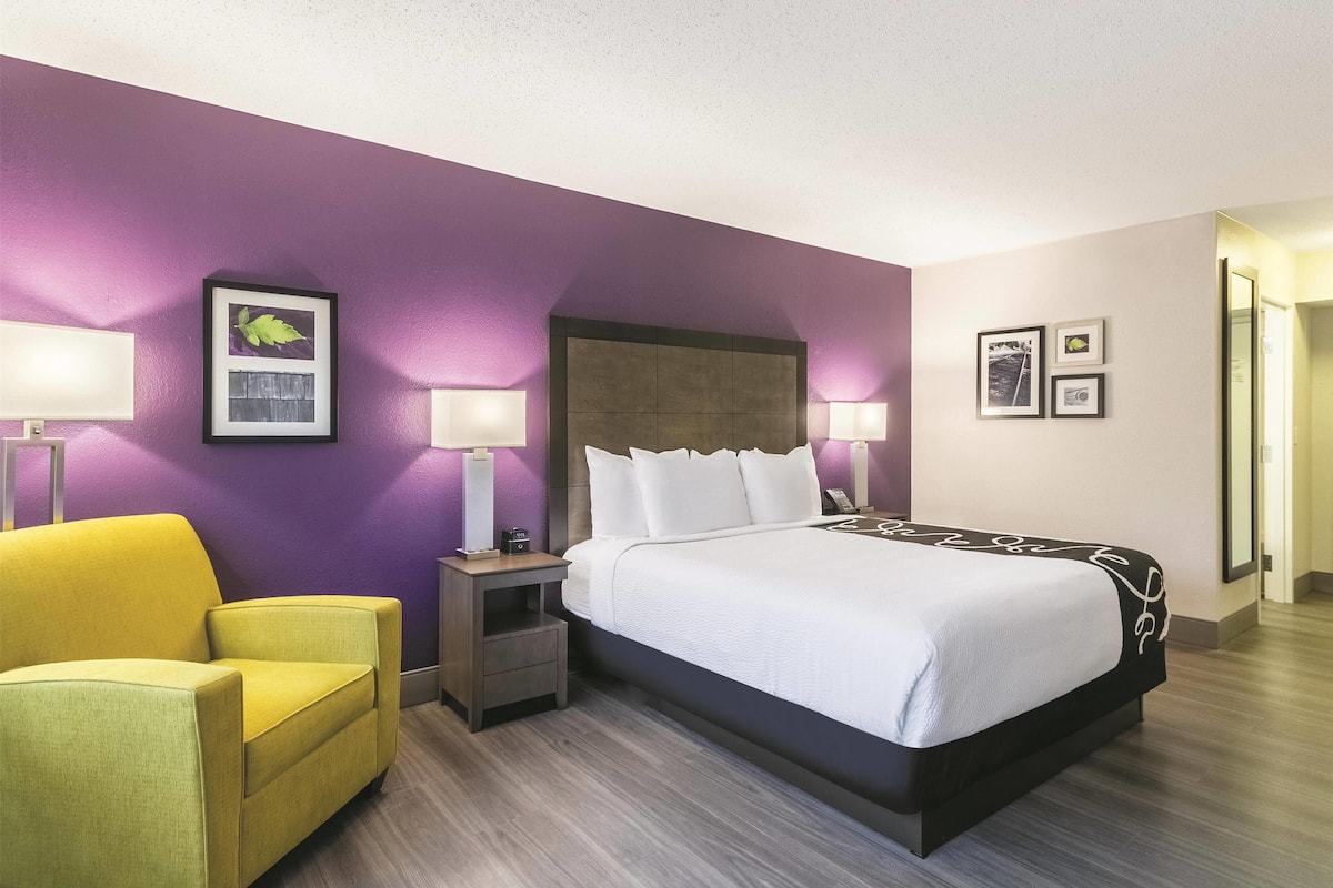 A hotel room with a bed, two bedside tables with lamps, a chair, and a wall with framed pictures.