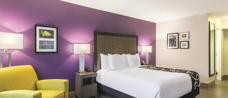 A hotel room with a bed, two bedside tables with lamps, a chair, and a wall with framed pictures.