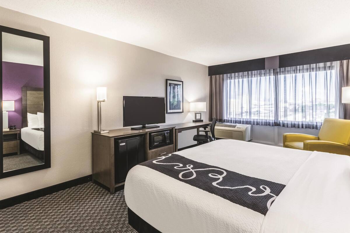 A hotel room with a bed, a desk, a TV, a chair, and a window with curtains.