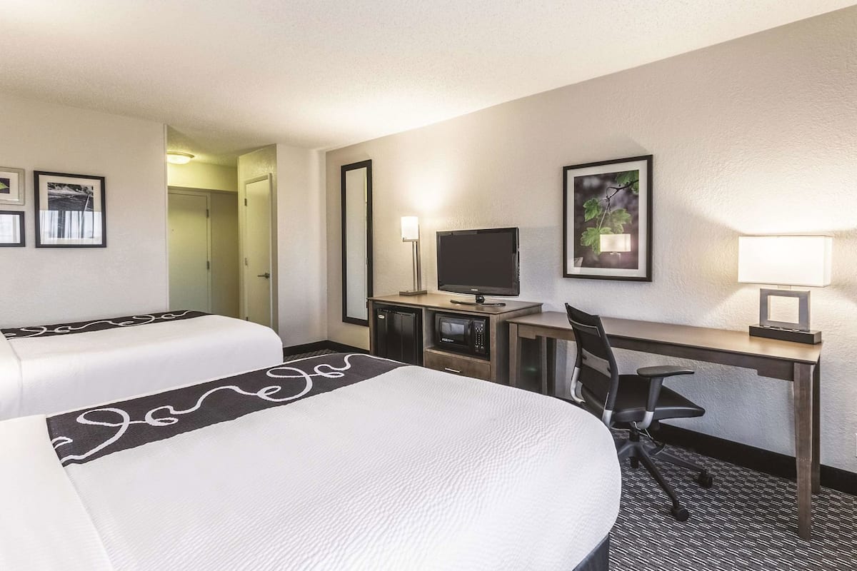 A hotel room with two beds, a desk with a computer and lamp, and a television.
