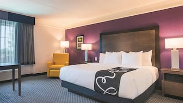 Una camera d'albergo con un letto grande, due abat-jour, una sedia e una finestra con tende.