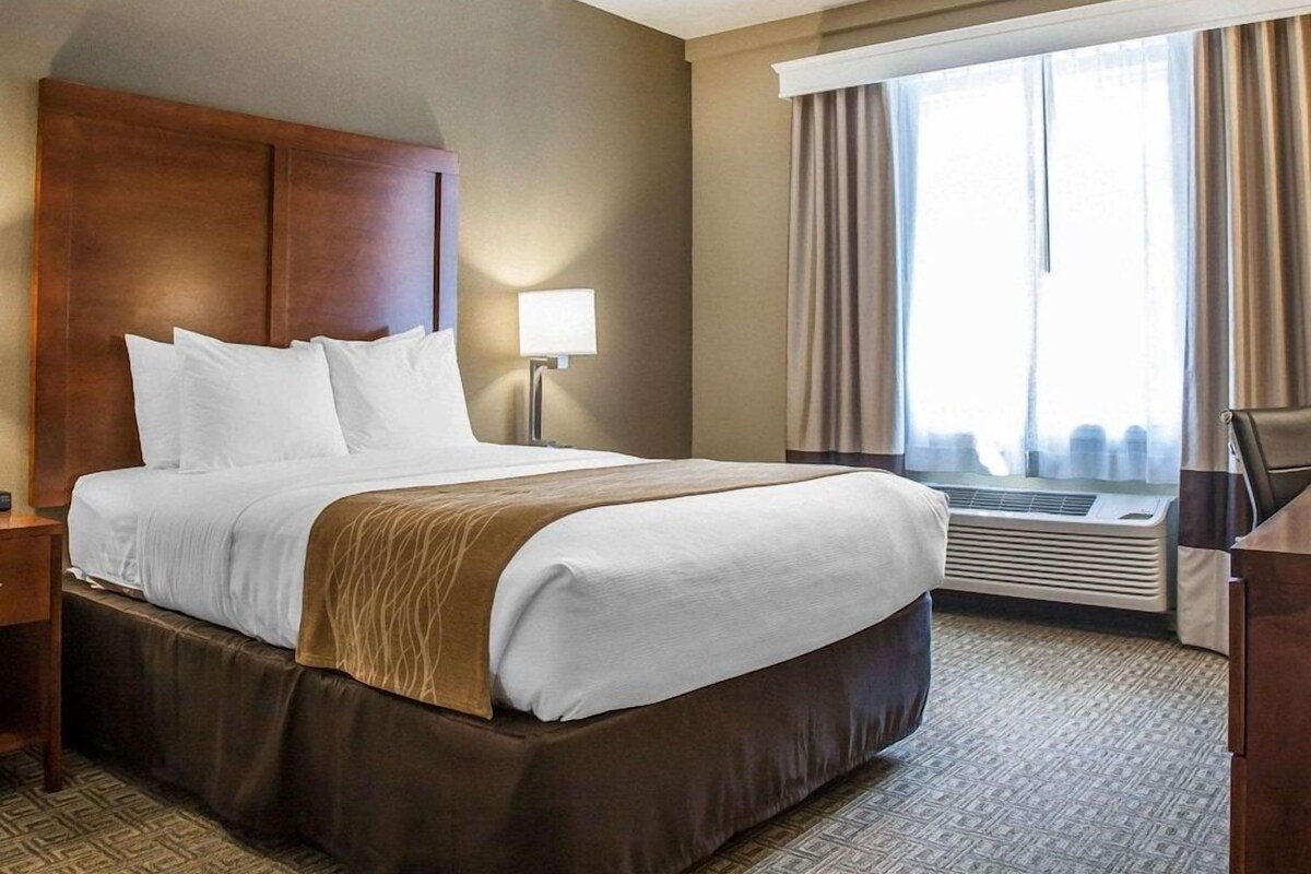 A hotel room with a large bed, a desk, a lamp, and a window with curtains.