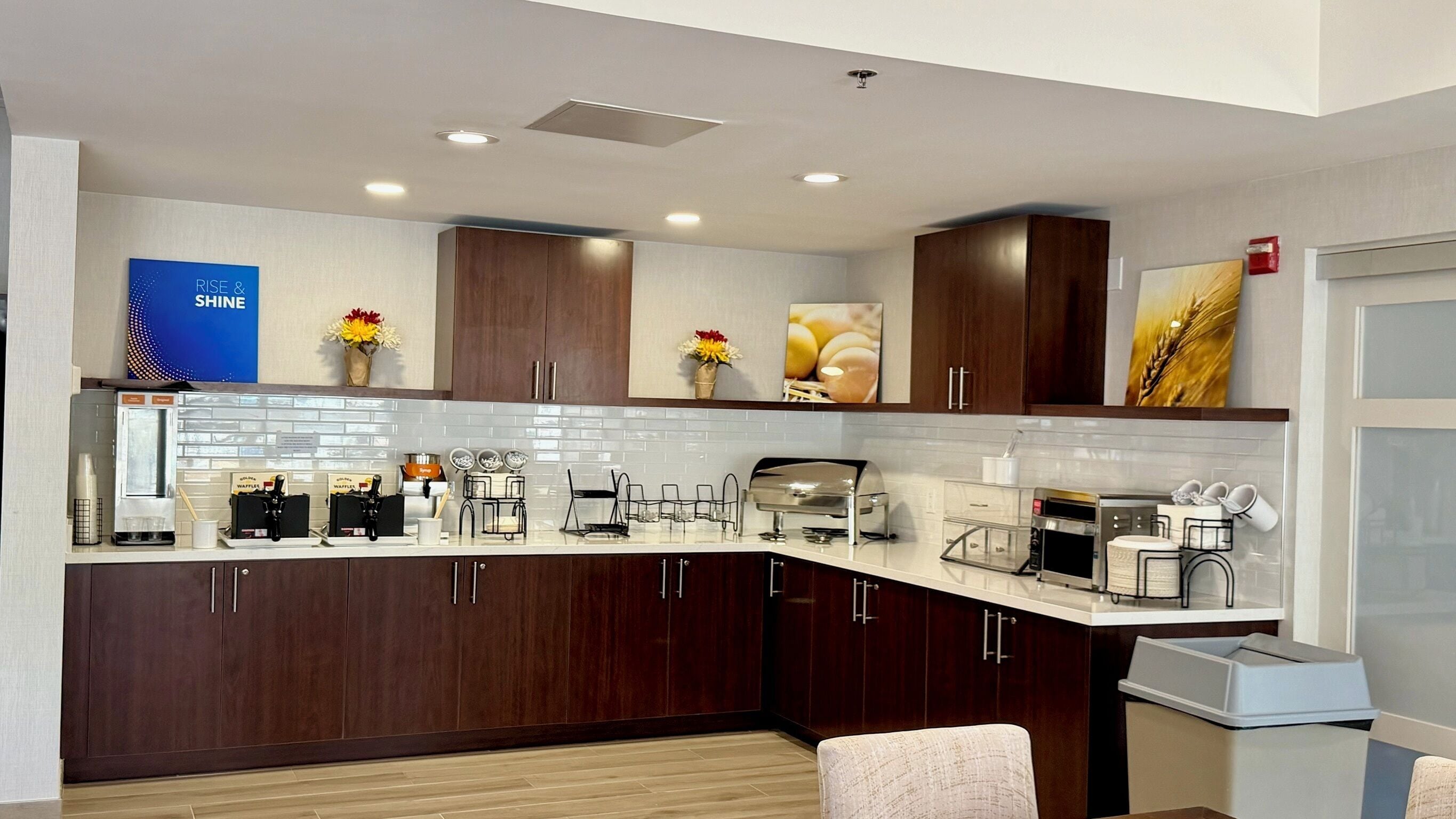 A modern kitchen with dark wood cabinets, white countertops, and various appliances including a coffee machine and toaster.