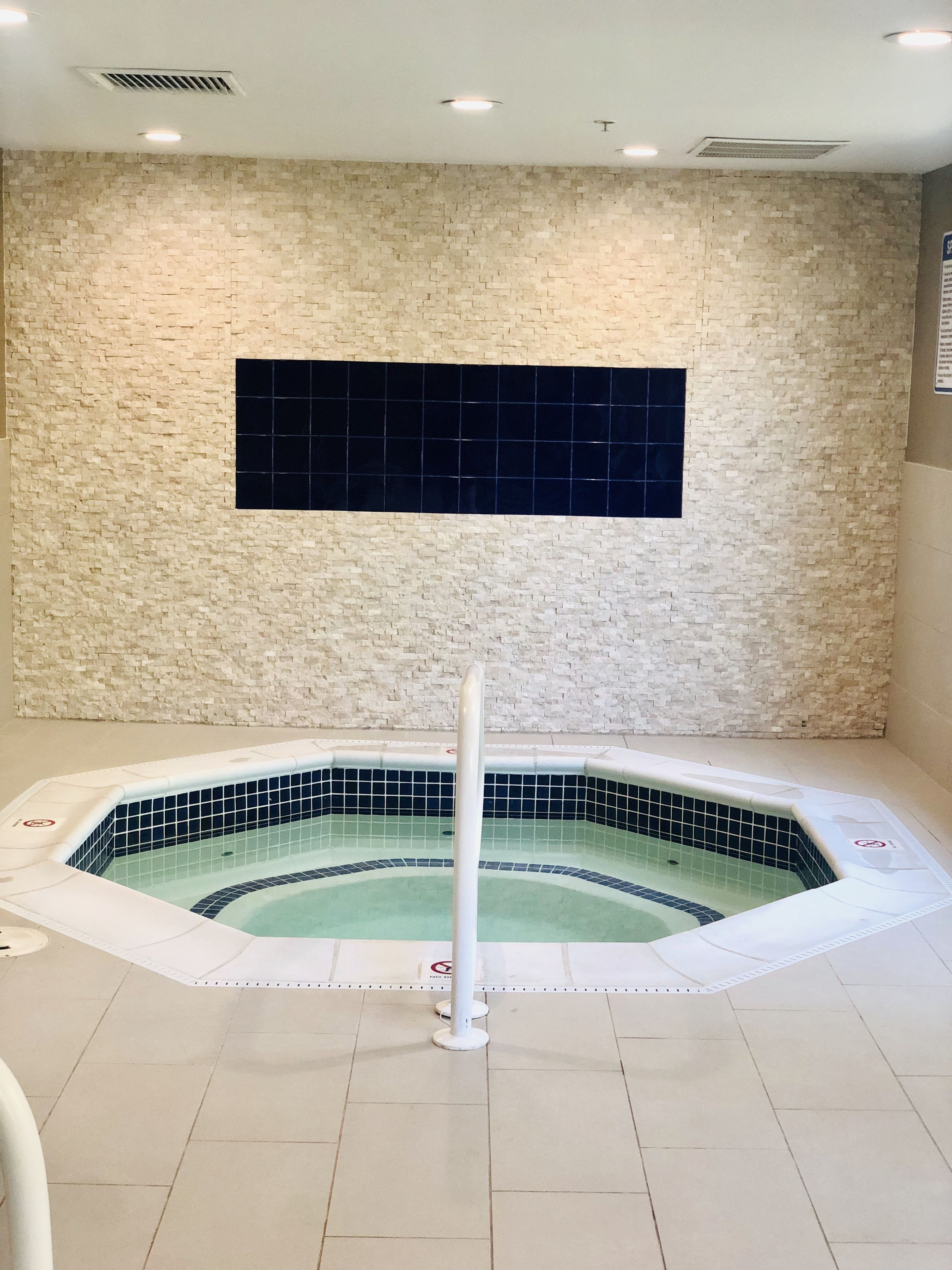 Un jacuzzi con suelo y paredes de baldosas, un poste blanco en el centro y un detalle de baldosa negra en la pared.