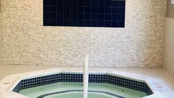 Un jacuzzi con suelo y paredes de baldosas, un poste blanco en el centro y un detalle de baldosa negra en la pared.